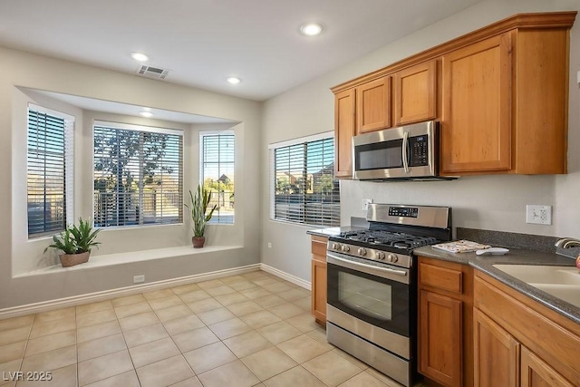 kitchen featuring recessed lighting, a sink, appliances with stainless steel finishes, brown cabinets, and dark countertops