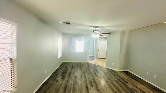 unfurnished room with baseboards, dark wood-type flooring, visible vents, and a ceiling fan