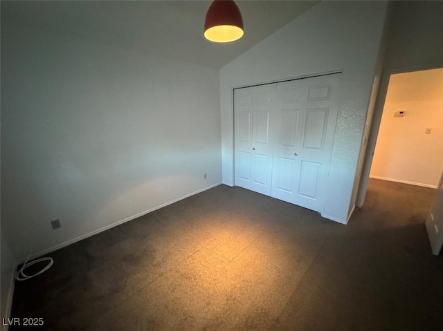 unfurnished bedroom featuring lofted ceiling, a closet, dark carpet, and baseboards