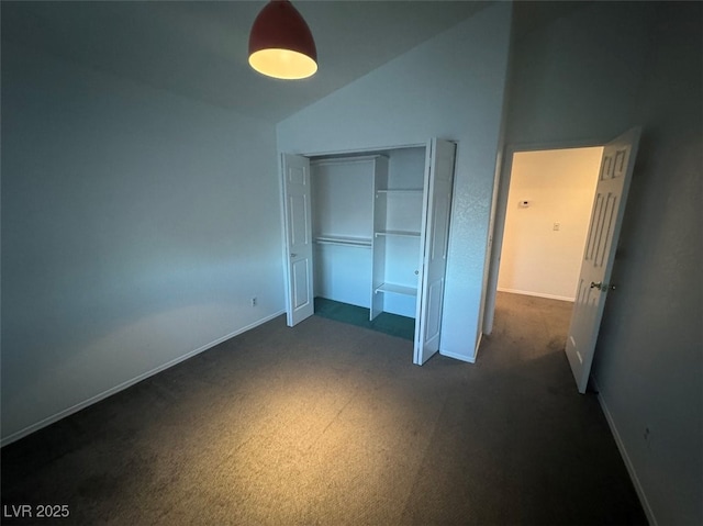 unfurnished bedroom with lofted ceiling, dark colored carpet, a closet, and baseboards