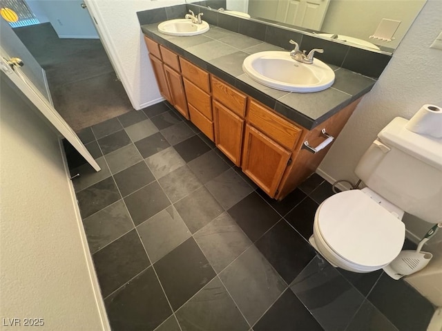 bathroom with double vanity, baseboards, toilet, and a sink