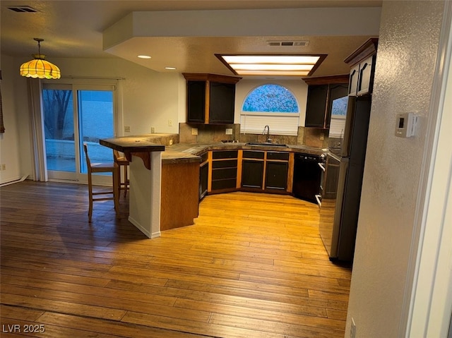 kitchen with a peninsula, a breakfast bar, a sink, visible vents, and black appliances