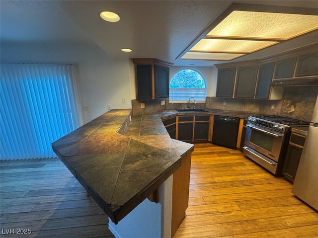 kitchen featuring black dishwasher, tile countertops, light wood-style flooring, gas range, and a peninsula