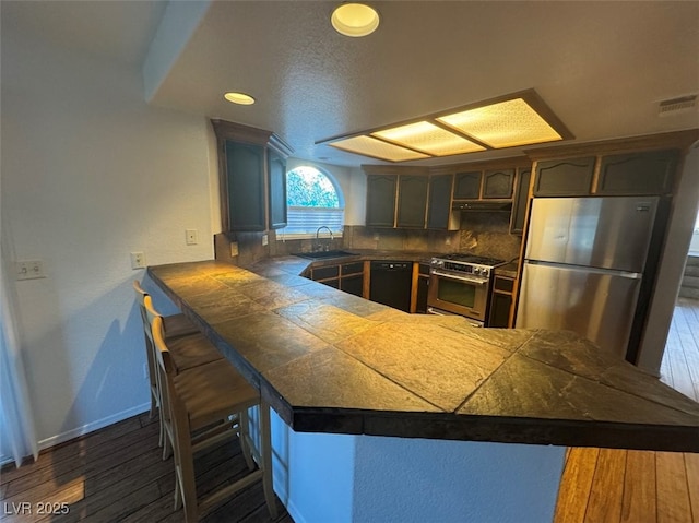 kitchen featuring tile countertops, a peninsula, a sink, visible vents, and appliances with stainless steel finishes