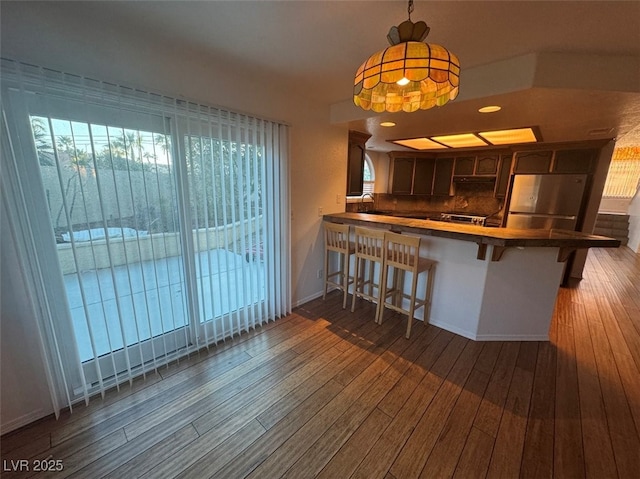 kitchen with a breakfast bar area, a peninsula, wood finished floors, dark brown cabinets, and stainless steel fridge