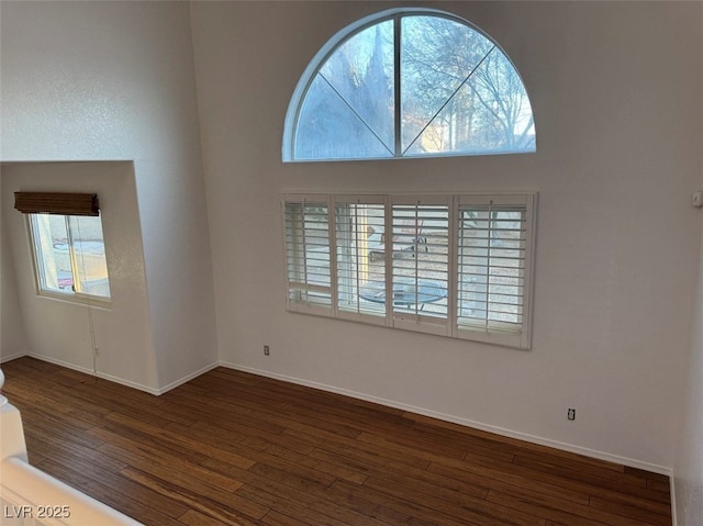 spare room with dark wood-type flooring, a towering ceiling, and baseboards