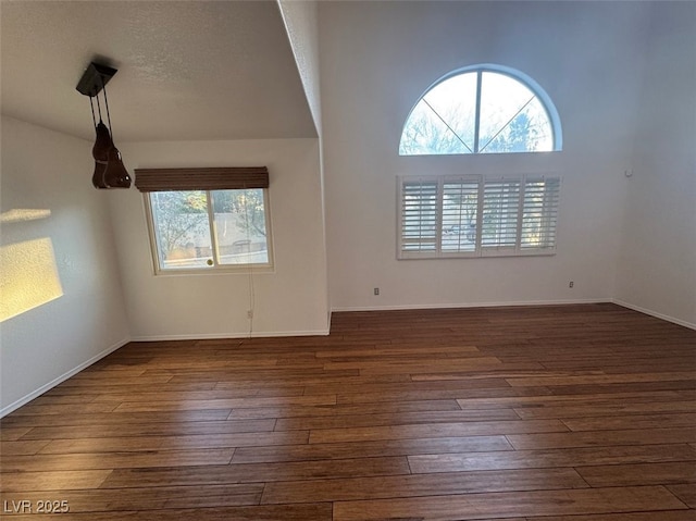 spare room with a textured ceiling, baseboards, and dark wood-style flooring