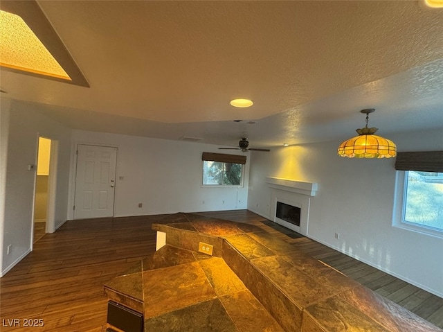 unfurnished living room with dark wood-style floors, a textured ceiling, a fireplace, and a healthy amount of sunlight