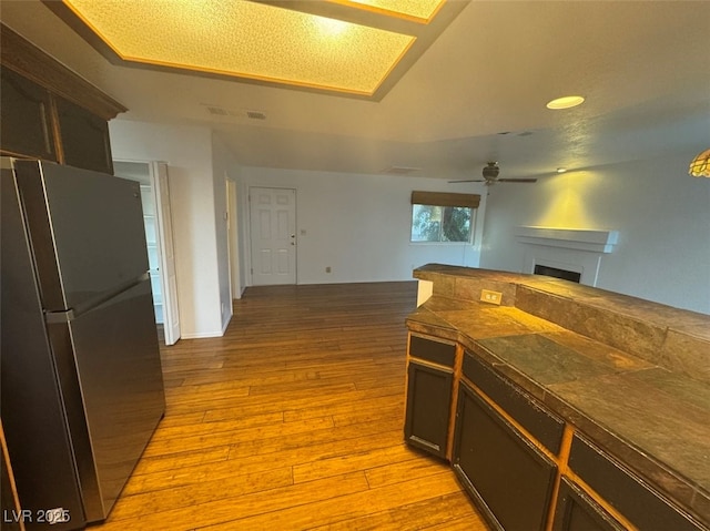 kitchen with ceiling fan, tile countertops, light wood-style flooring, a fireplace, and freestanding refrigerator