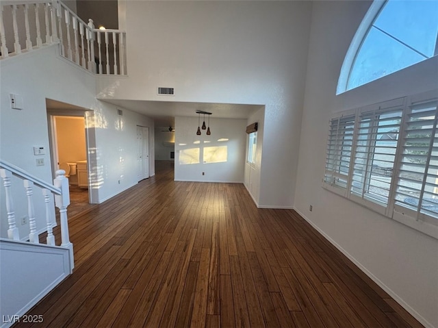 unfurnished living room featuring dark wood-style floors, visible vents, stairway, a towering ceiling, and baseboards