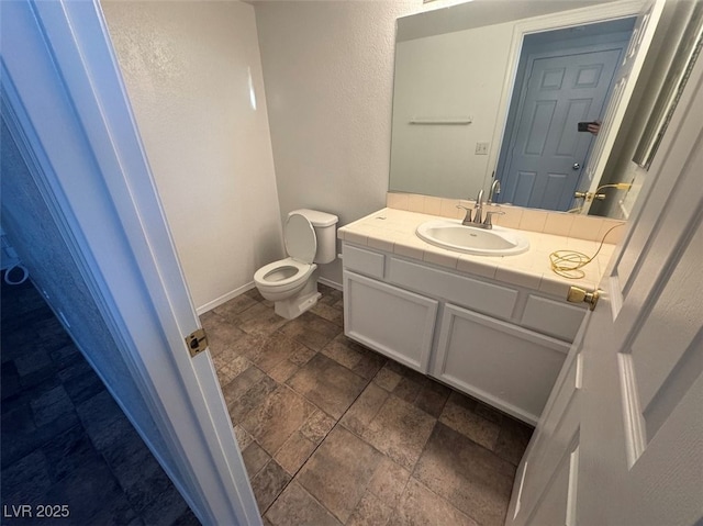 half bathroom with stone finish floor, toilet, vanity, and baseboards