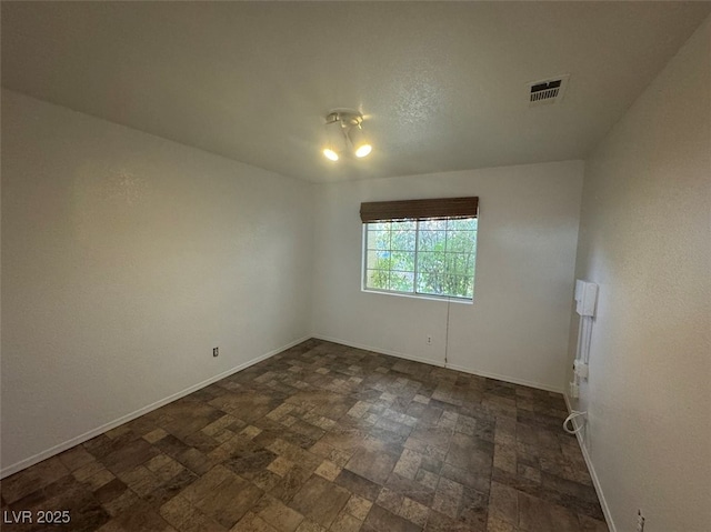 unfurnished room featuring stone finish flooring, visible vents, and baseboards