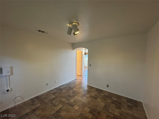 empty room with arched walkways, stone finish flooring, visible vents, and baseboards