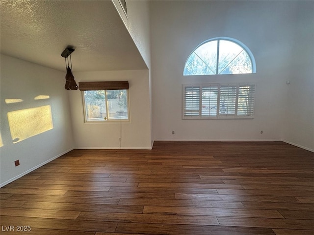 spare room featuring a textured ceiling, dark wood-style flooring, and baseboards