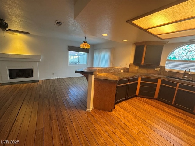 bar featuring a fireplace, light wood finished floors, visible vents, a ceiling fan, and a sink