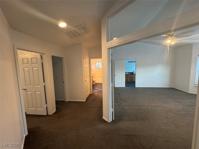 hall with lofted ceiling, dark carpet, visible vents, and baseboards