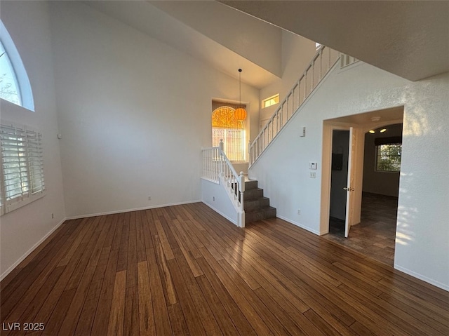 unfurnished living room with stairs, high vaulted ceiling, and dark wood finished floors