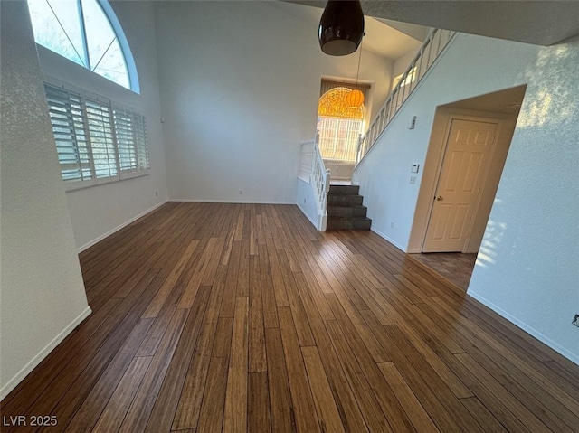 unfurnished living room with dark wood-style floors, baseboards, a high ceiling, and stairs