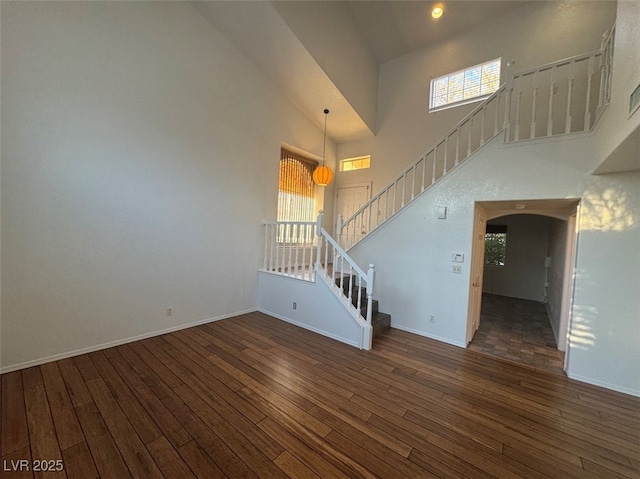 interior space featuring stairway, dark wood-style flooring, a towering ceiling, and baseboards