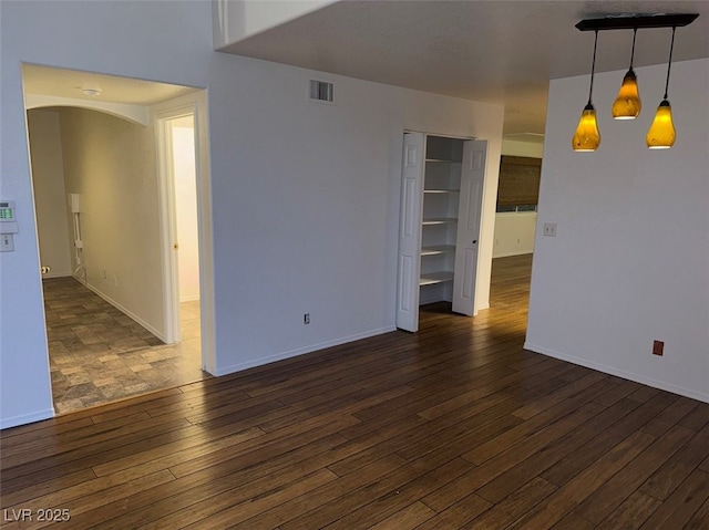 spare room featuring baseboards, visible vents, dark wood finished floors, and arched walkways