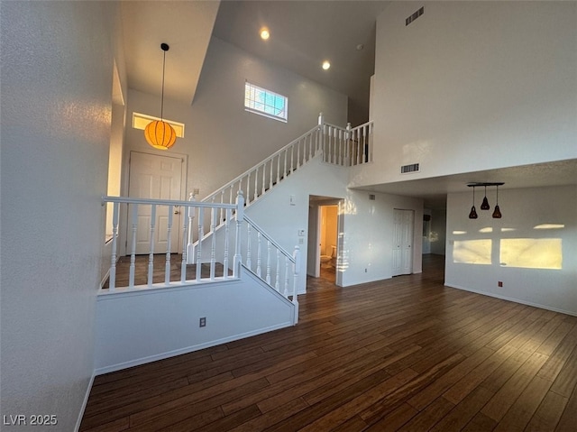 unfurnished living room with dark wood-style flooring, visible vents, a high ceiling, and stairs