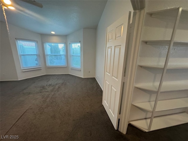 spare room with a textured ceiling, dark colored carpet, and baseboards