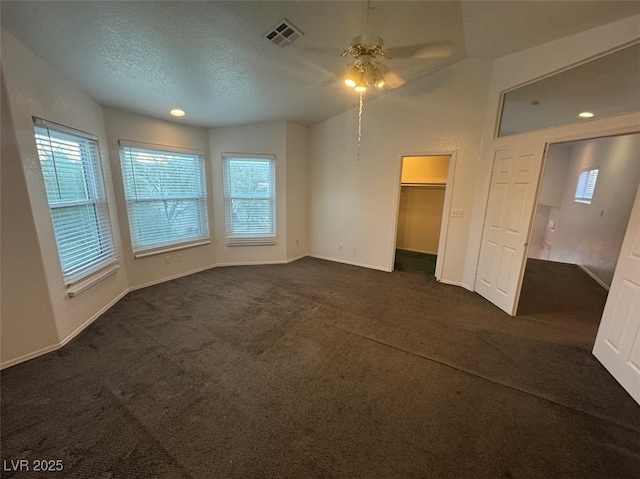 interior space with vaulted ceiling, dark colored carpet, a textured ceiling, and visible vents