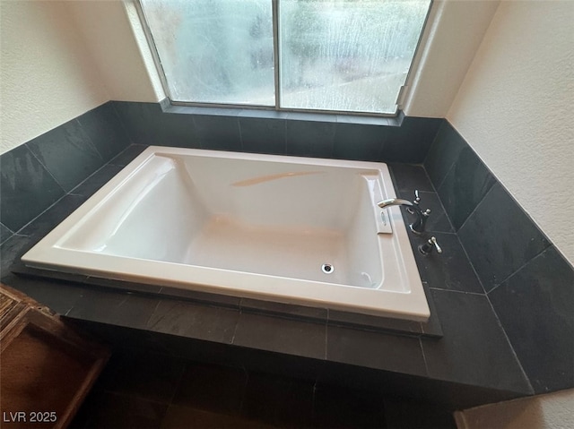 full bath featuring a textured wall, a garden tub, and a healthy amount of sunlight