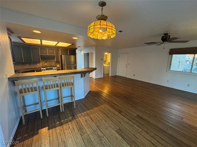 kitchen featuring dark wood-style floors, a breakfast bar, freestanding refrigerator, dark brown cabinetry, and a peninsula