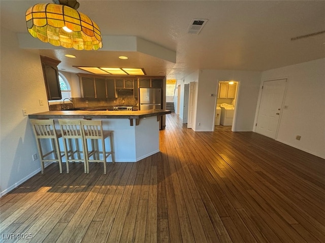 kitchen with a peninsula, a sink, a kitchen breakfast bar, washer and clothes dryer, and stainless steel fridge