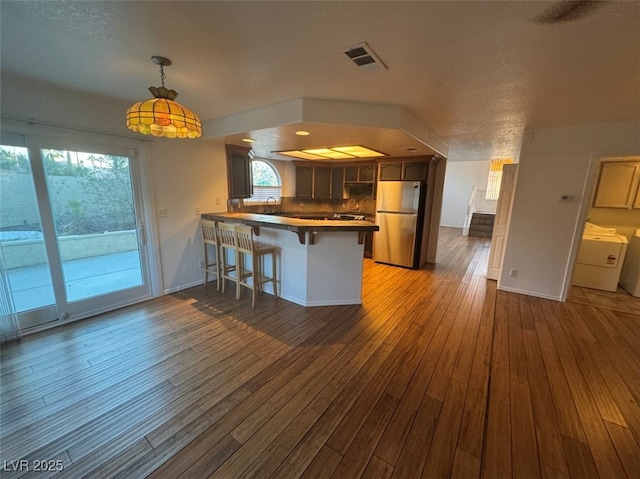 kitchen featuring visible vents, freestanding refrigerator, wood finished floors, a peninsula, and a kitchen bar