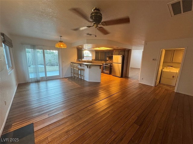 interior space featuring a breakfast bar area, a peninsula, visible vents, freestanding refrigerator, and washer / clothes dryer