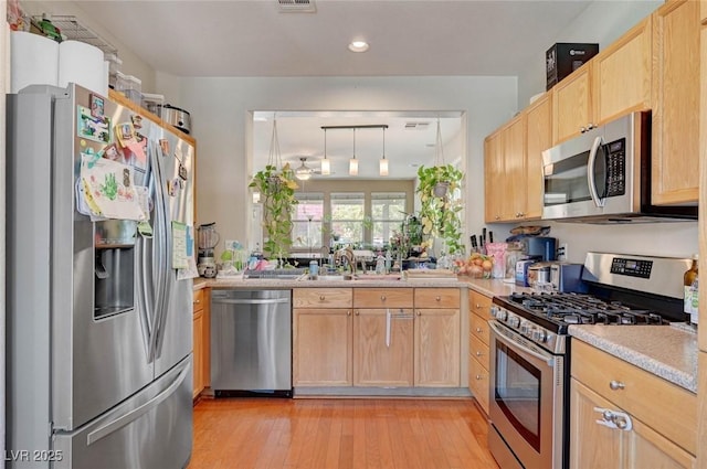 kitchen with light countertops, light brown cabinetry, appliances with stainless steel finishes, light wood-style floors, and a sink