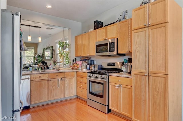 kitchen featuring appliances with stainless steel finishes, hanging light fixtures, light countertops, light wood-style floors, and light brown cabinets