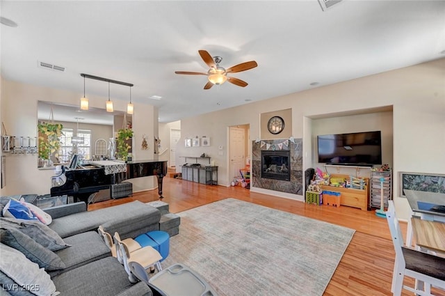 living room featuring a ceiling fan, a fireplace, visible vents, and light wood-style floors