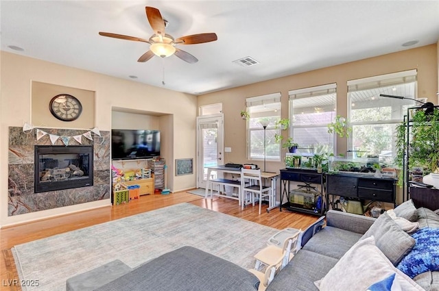 living room with light wood finished floors, a premium fireplace, visible vents, and a ceiling fan