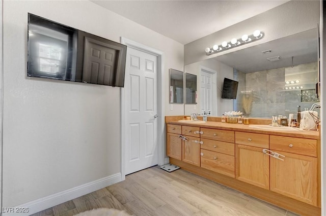 bathroom with double vanity, baseboards, a sink, and wood finished floors