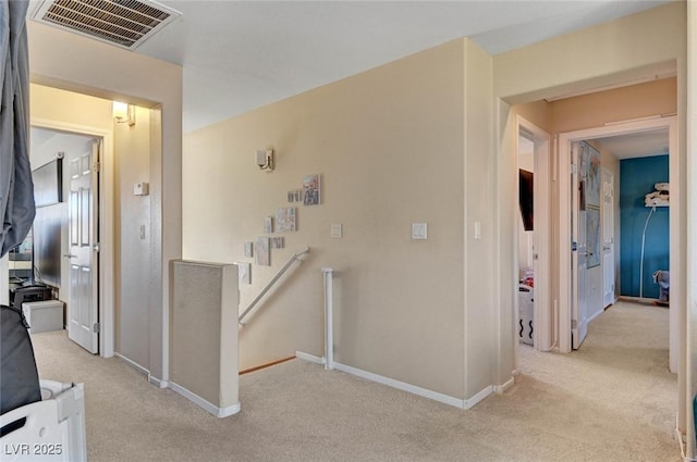 hallway featuring baseboards, visible vents, light colored carpet, and an upstairs landing