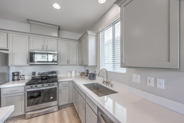 kitchen with light stone counters, gray cabinetry, stainless steel appliances, a sink, and light wood-type flooring