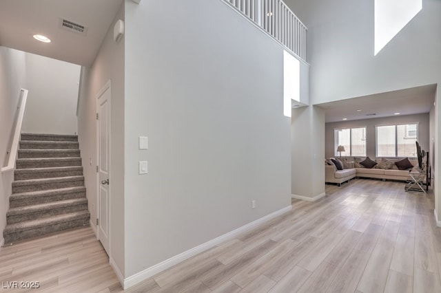 interior space featuring a towering ceiling, visible vents, baseboards, stairway, and light wood finished floors