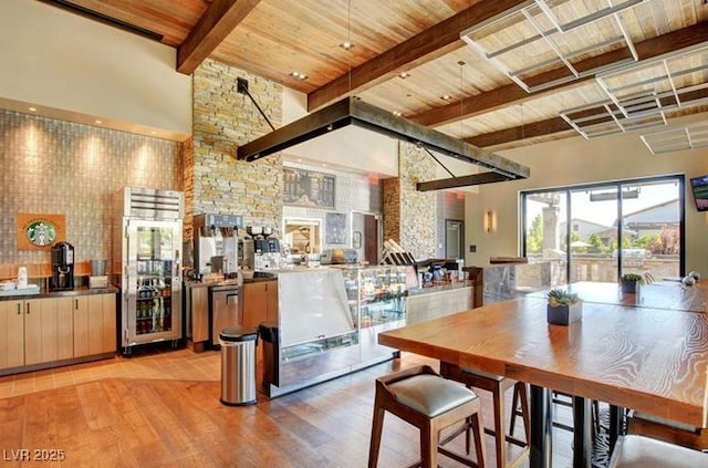 dining room featuring a community bar, a towering ceiling, wooden ceiling, light wood-style floors, and beam ceiling