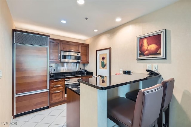 kitchen featuring light tile patterned floors, dark countertops, a breakfast bar, a peninsula, and stainless steel appliances