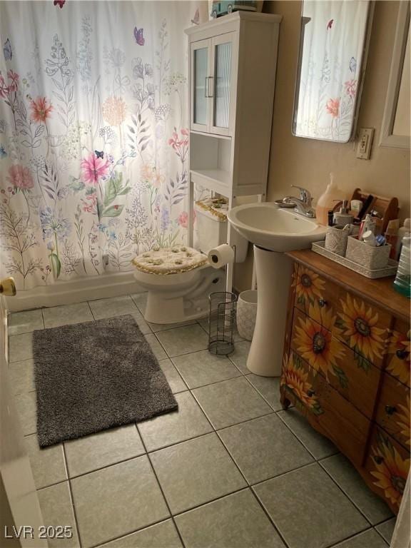 bathroom with baseboards, toilet, shower / tub combo with curtain, tile patterned flooring, and a sink