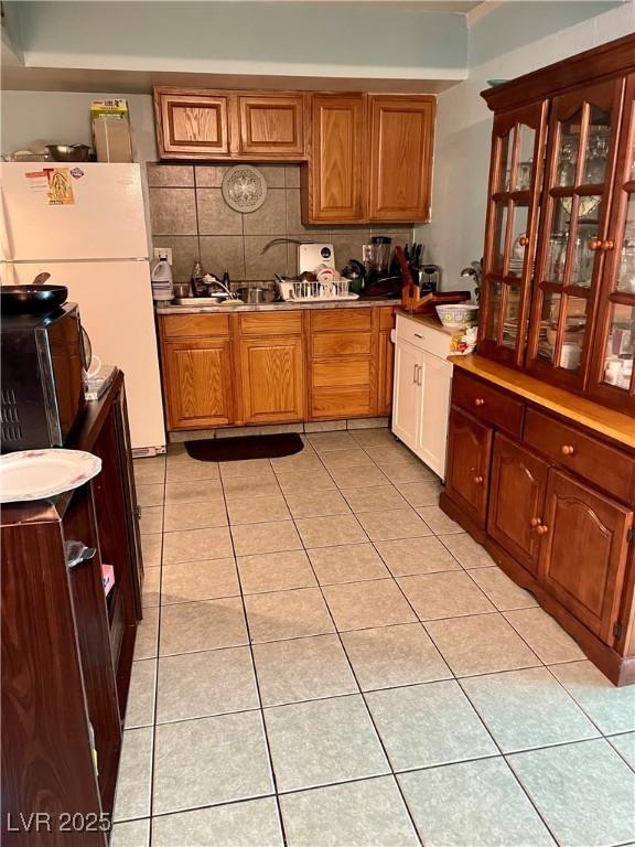 kitchen featuring light tile patterned floors, brown cabinetry, backsplash, and freestanding refrigerator