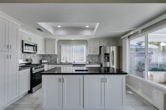 kitchen with visible vents, a raised ceiling, white cabinets, dark countertops, and appliances with stainless steel finishes