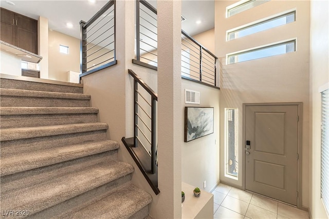 entryway with visible vents, a high ceiling, light tile patterned flooring, baseboards, and stairs