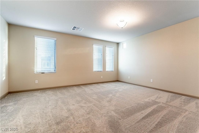 spare room featuring baseboards, a wealth of natural light, visible vents, and light colored carpet