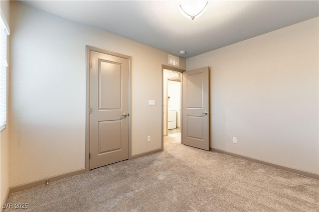 unfurnished bedroom with washer / dryer, light carpet, visible vents, and baseboards