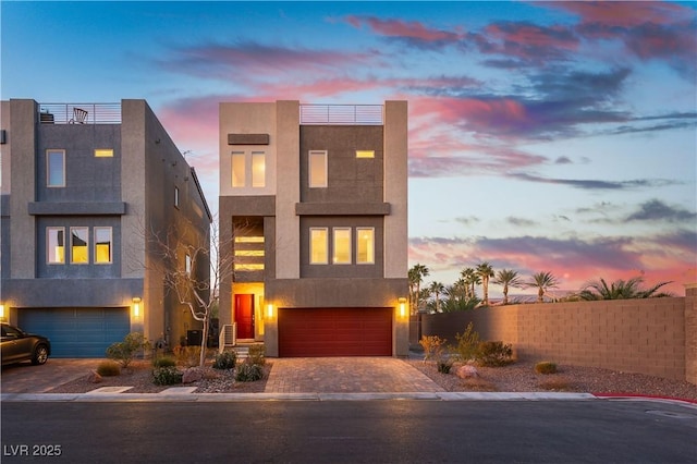 modern home with decorative driveway, fence, an attached garage, and stucco siding