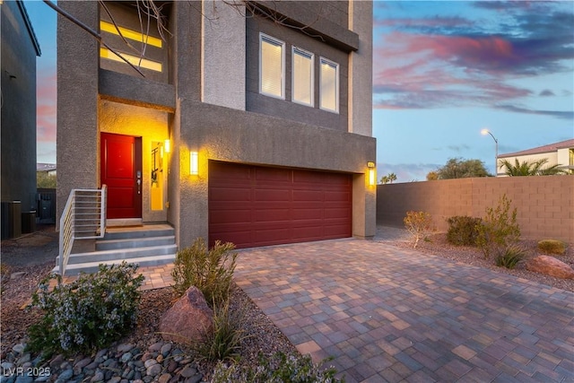 view of front of property with decorative driveway, fence, an attached garage, and stucco siding